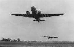 A C-47 Skytrain of the 438<sup>th</sup> Troop Carrier Group tugs a glider, as it takes off from Greenham Common on D-Day, June 6, 1944. American Air Museum in Britain (FRE 3381).