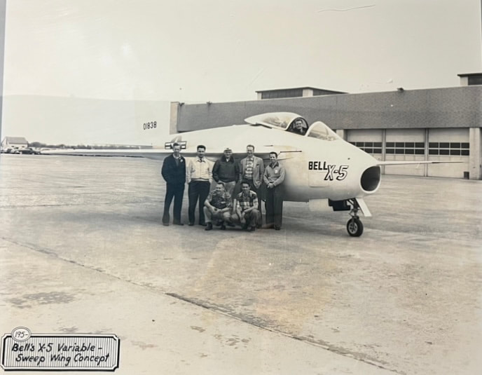 Seven men are standing in front of a Bell X5 plane.