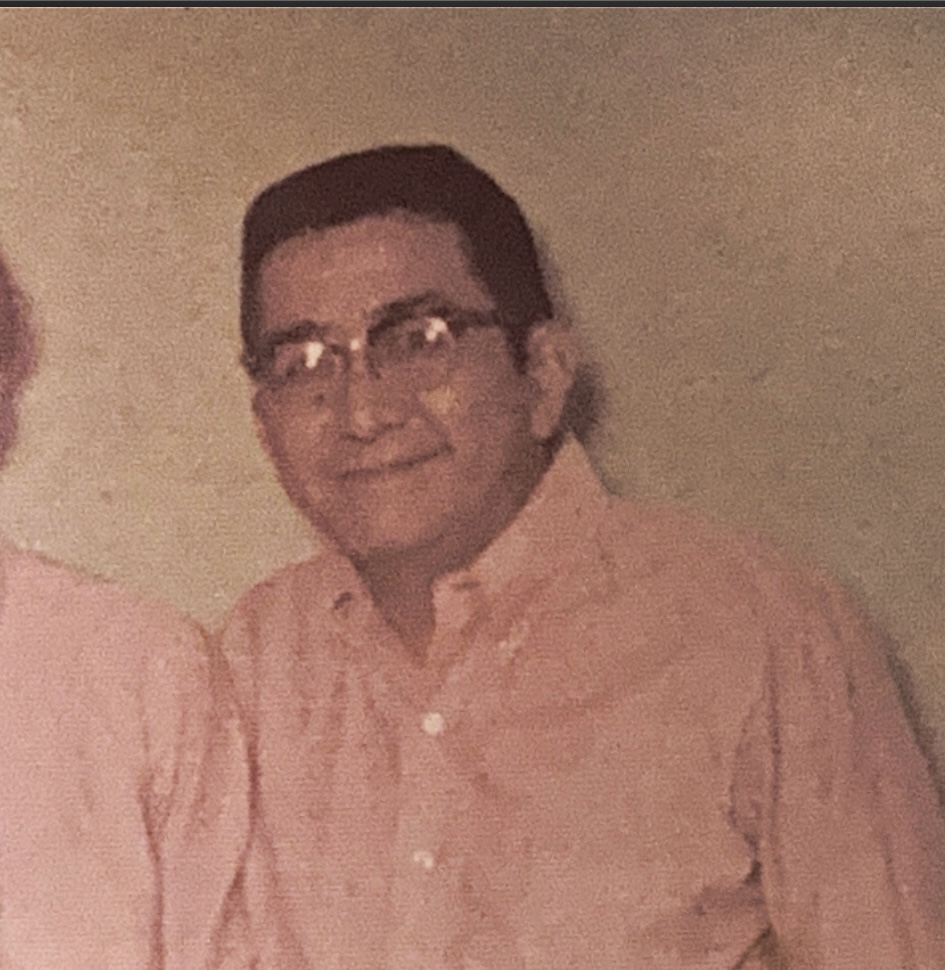 Reginald Arakaki as a veteran, wearing a pink button-up shirt and glasses.