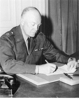 President Eisenhower, in uniform, sits at a table signing the activation order for SHAPE.