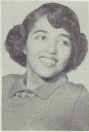Mcintyre looks over her left shoulder. She is smiling and dressed up in a sweater and collared shirt