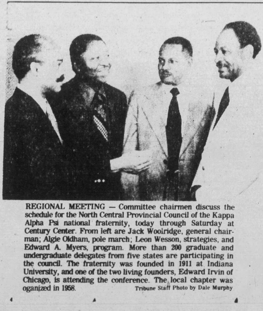 Four men in suits and ties are standing close to one another and are engaged in a discussion.
