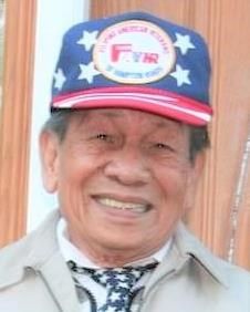 An older man is smiling and looking directly at the camera. He is wearing an American flag inspired hat and tie.