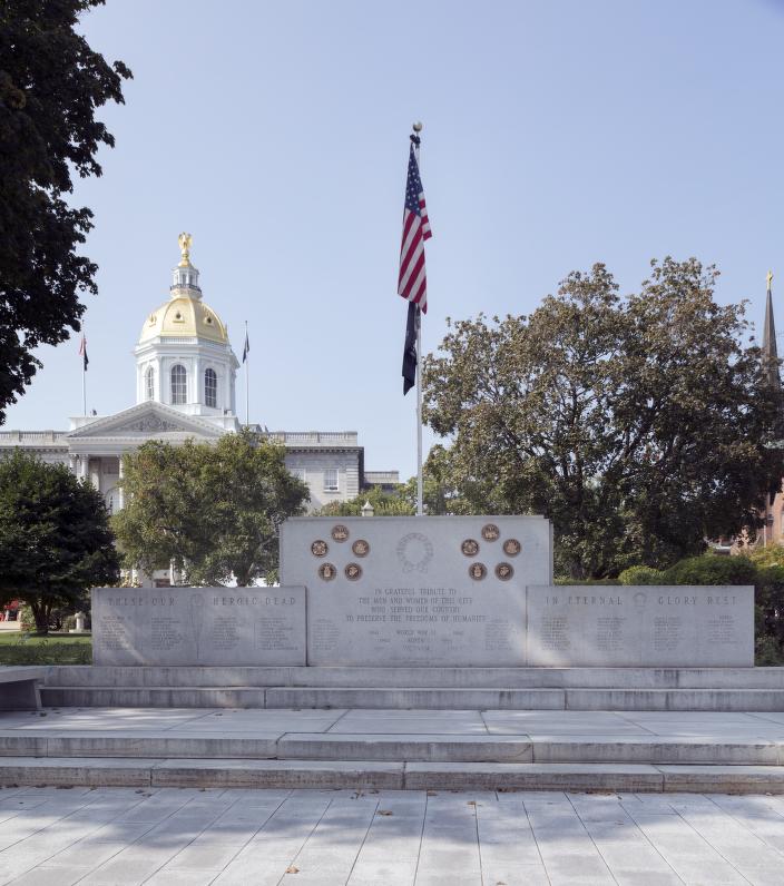 Photo of a military monument with a flag in the center and a horse statue in the rear left background.