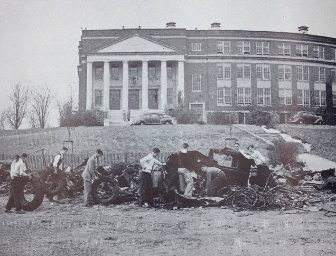 Black and White photo students standing in front of a school with piles of metal scrap.
