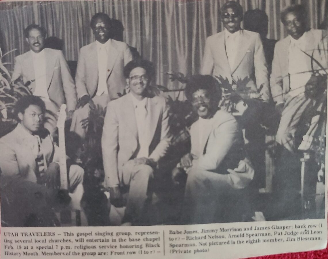ALT: Seven African American men are in matching suits standing on a stage with their instruments. It is a black and white photograph from a newspaper.