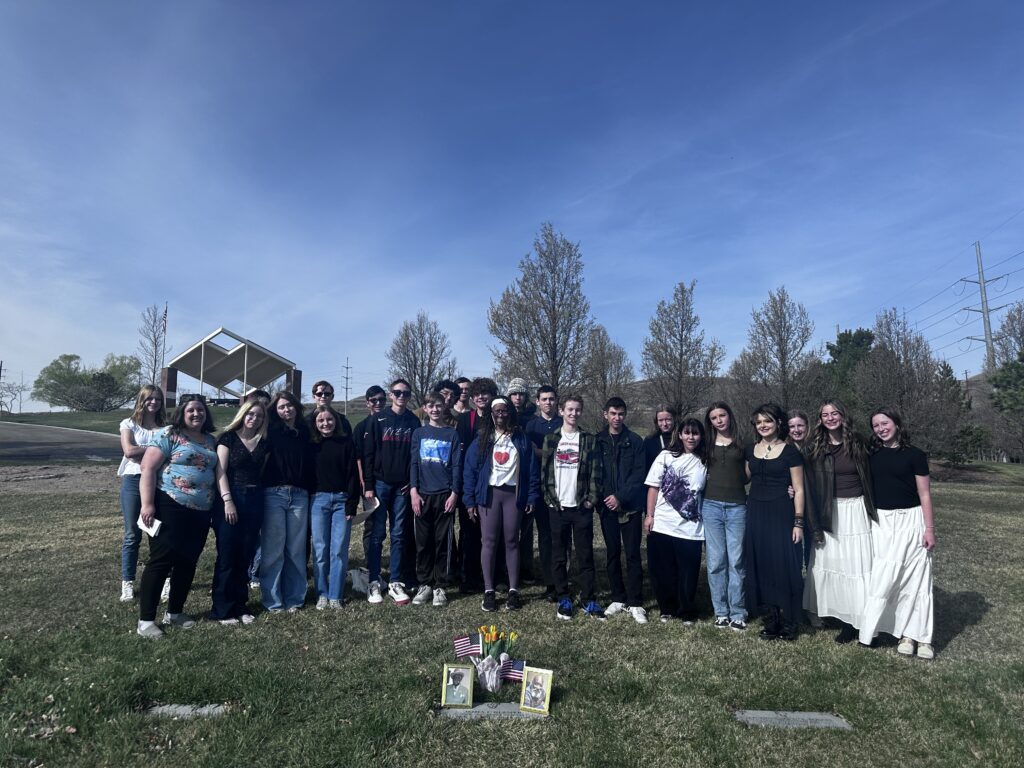 A large group of students and family members stand around Glasper’s grave marker.