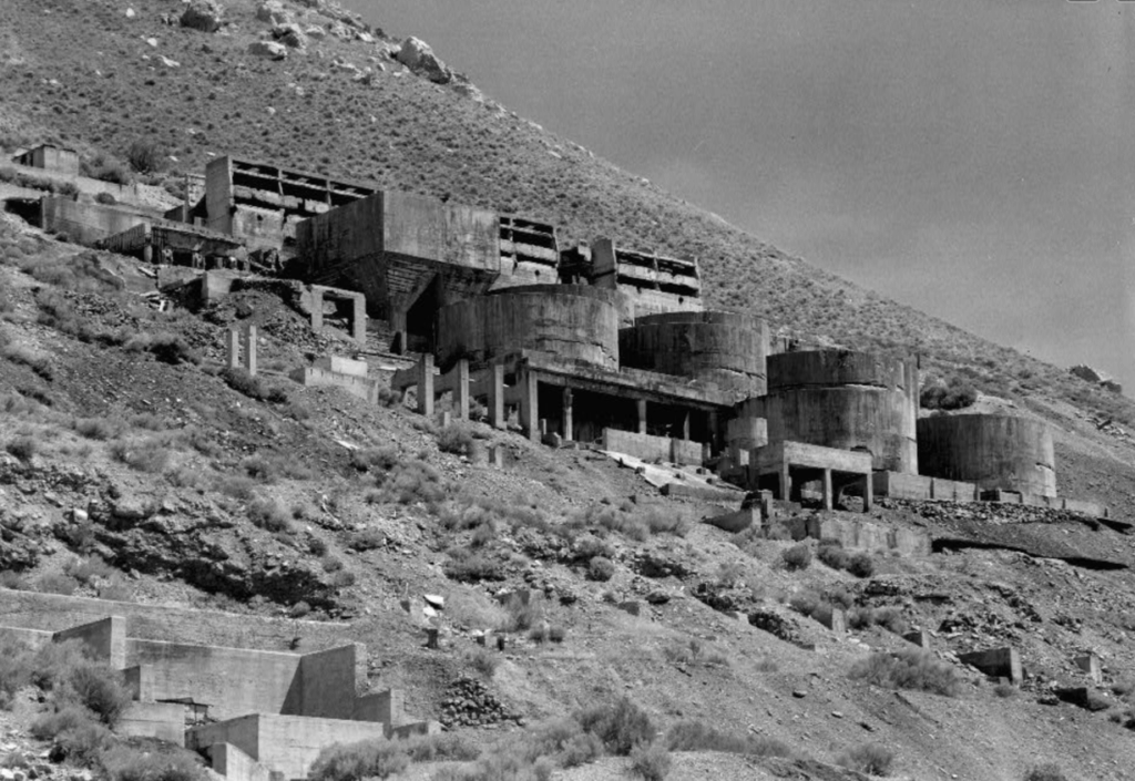 A black and white photo of several concrete structures on the side of a mountain.