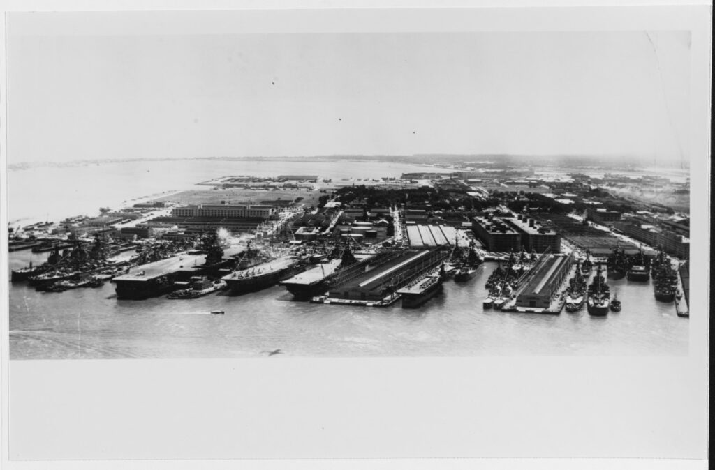 An aerial black and white photograph of several ships along multiple docks.