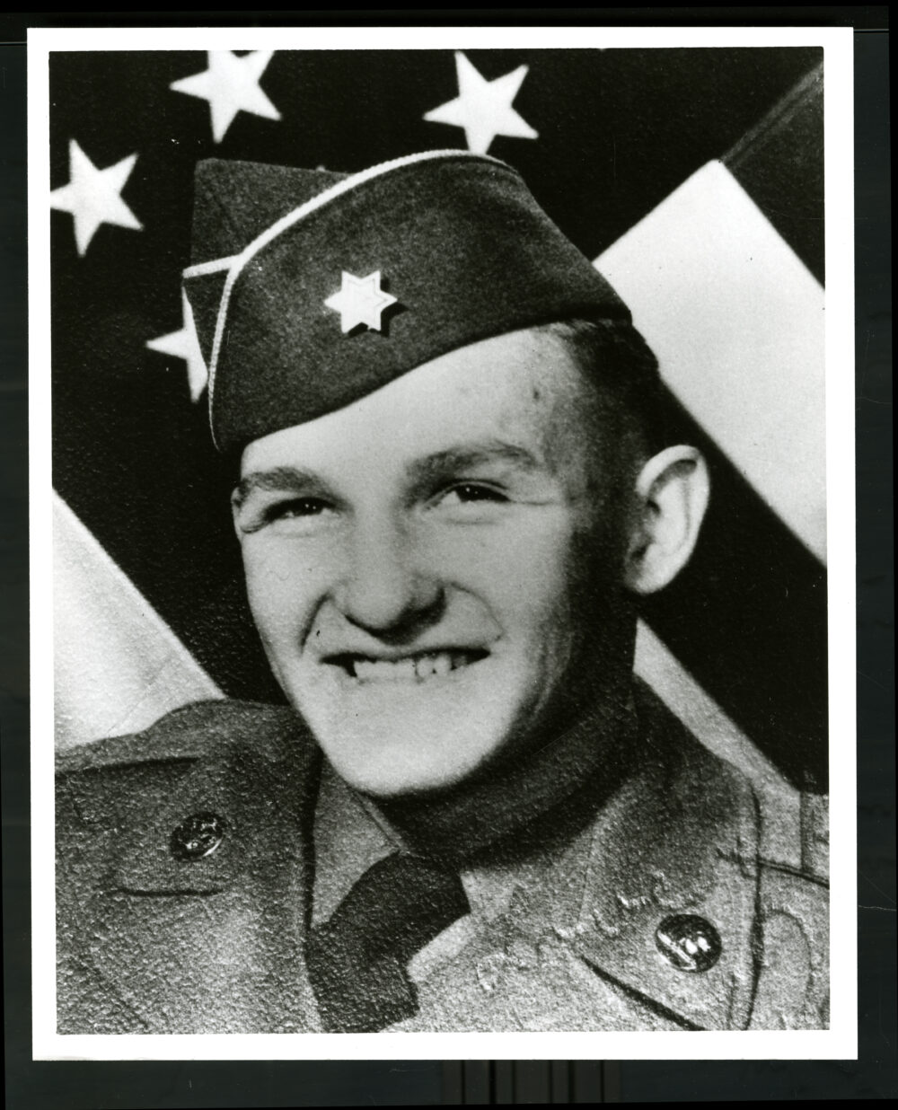 Dan Schoonover, smiling in his Army uniform in front of an American flag.
