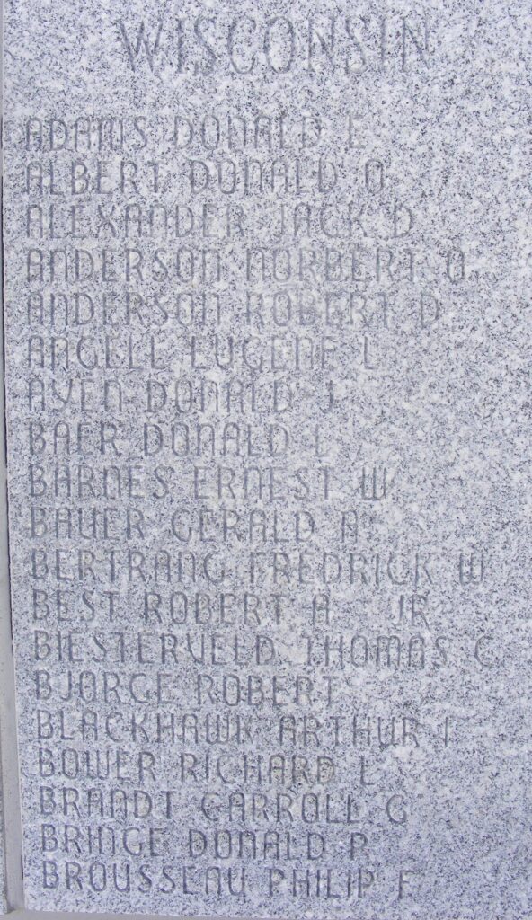 An image of a gray marble wall engraved with ‘Wisconsin Adams Donald E’ among other names.
