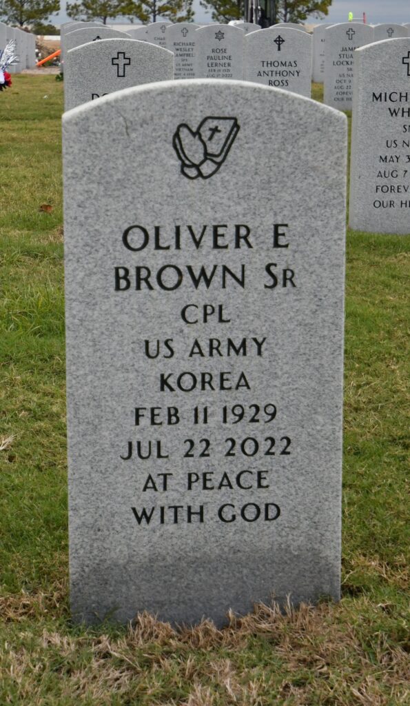 An arch-topped marble marker engraved with praying hands and a bible on top and then the words “Oliver E Brown SR CPL US Army Korea Feb 11 1929 JUL 22 2022 At Peace With God.”