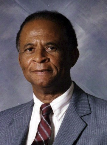 A headshot of an older Black man is dressed in a blue, pin-striped suit jacket, white button-up shirt, and a maroon striped tie.