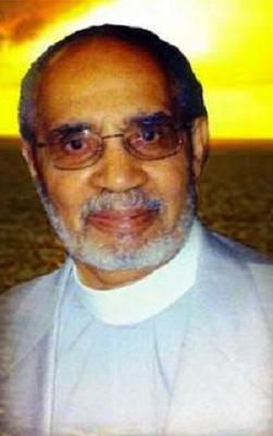 A color headshot of an elderly African American man. He has a beard and is wearing glasses and a clerical collar.