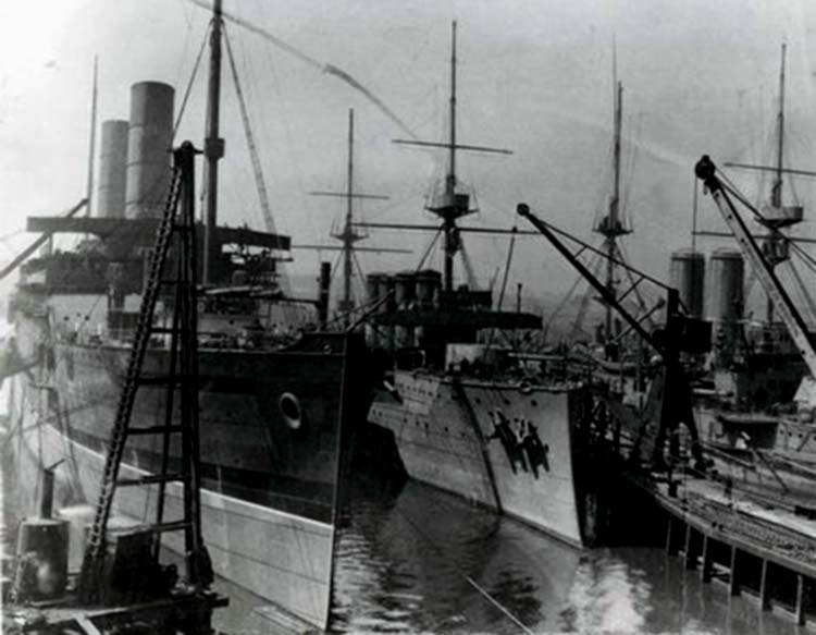 A black and white image of three ships being worked on in a dock.