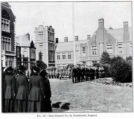A black and white image of men and women in uniform and in formation outside of several baroque-style buildings.
