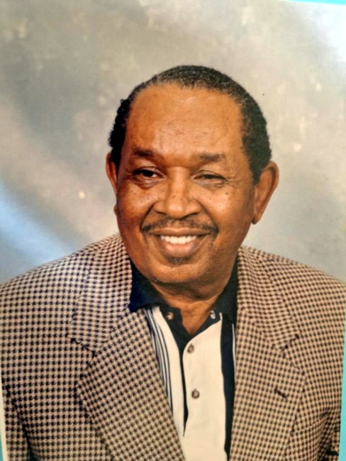 An older African American man wearing a plaid jacket.