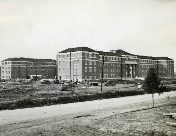 A black and white image of four-story brick buildings surrounded by land-work being completed.