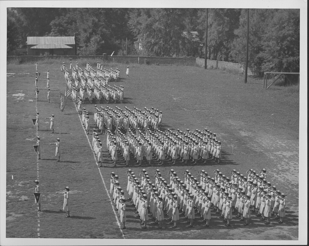 A black and white aerial photo of several dozen women standing in rows in their uniforms.