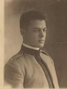A young man in a military-style jacket facing right.