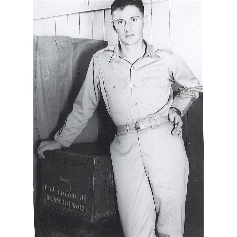 A young man in military uniform leaning on foot locker.