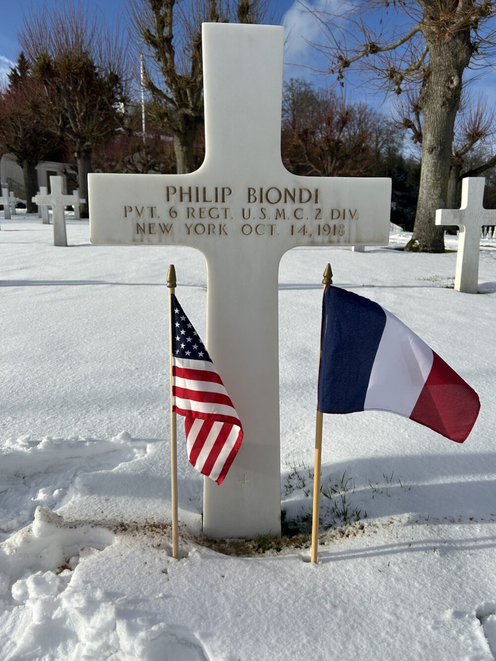 Philip Biondi's grave at Suresnes American Cemetery with French and American flags in the snow.