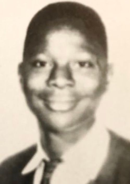 A black and white headshot photo of a young African-American man in a suit and tie. He is smiling at the camera. 