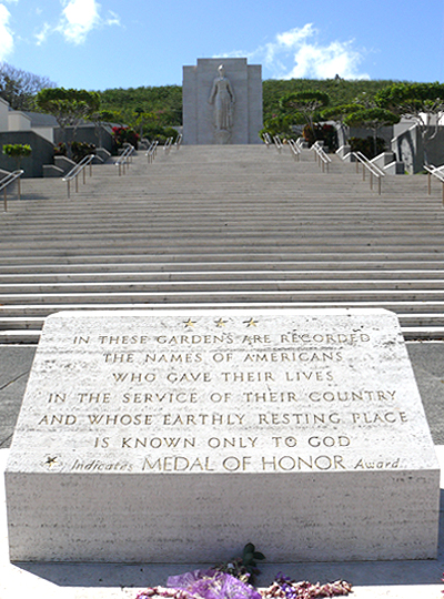 A white marble stone at the foot of the stairs looking up to a marble sculpture. The engraving reads, “In these gardens are recorded the names of Americans who gave their lives in the service of their country and whose Earthly resting place is known only to God.”