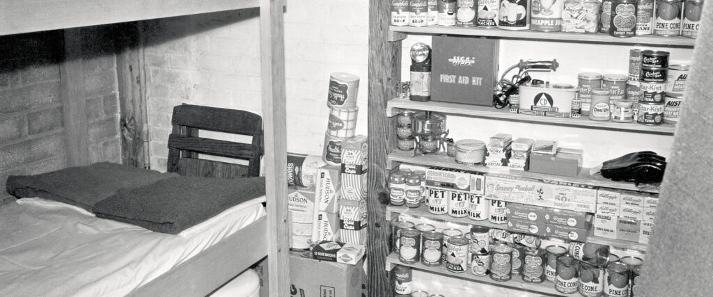 A black and white photo shows multiple shelves filled with canned goods and other supplies. Also pictured is a bunk bed.