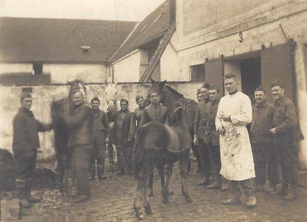 A sepia photograph of several men standing around outside in a village with a horse.