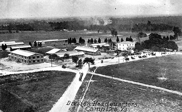 A black and white aerial photograph showing several buildings in the middle of empty fields. There are some trees around, but mostly empty fields. 