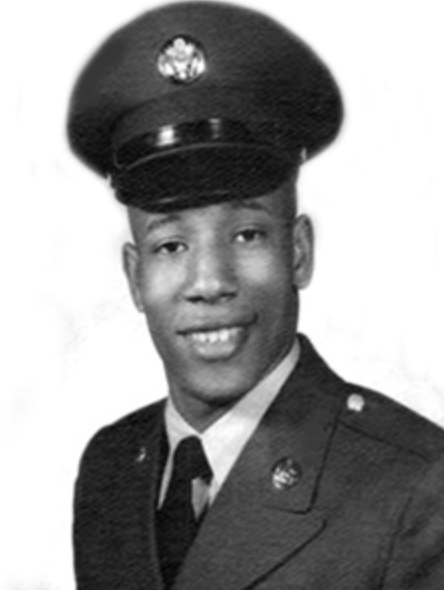 Black and white headshot of a young Black man in a military uniform. He is smiling at the camera.