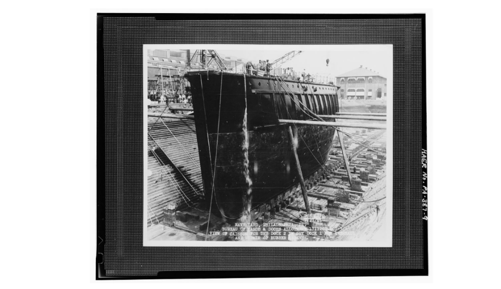 A black and white image of a ship in dry dock being worked on.