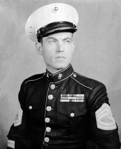 A black and white photograph of a young White man in a Marine uniform. He is photographed from the stomach up and is looking off to the side.