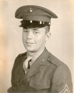 Sepia photo of a young White man from the chest up in his military uniform. He is smiling at the camera.
