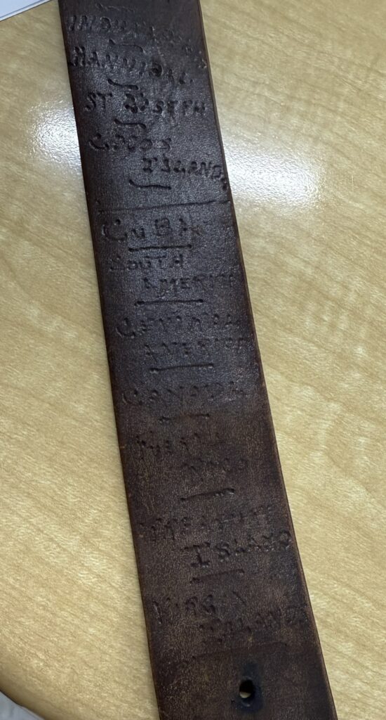 A color image of a dark brown leather belt with different inscribed locations. 