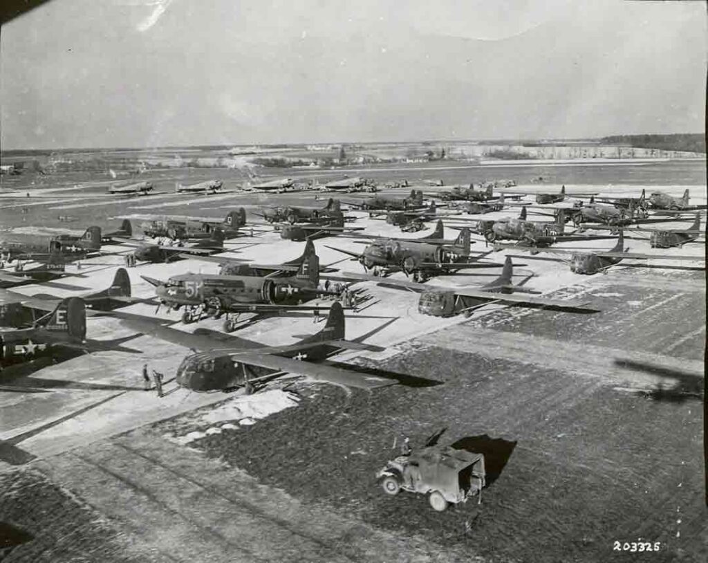 A black and white image of several airplanes lined up on a runway.