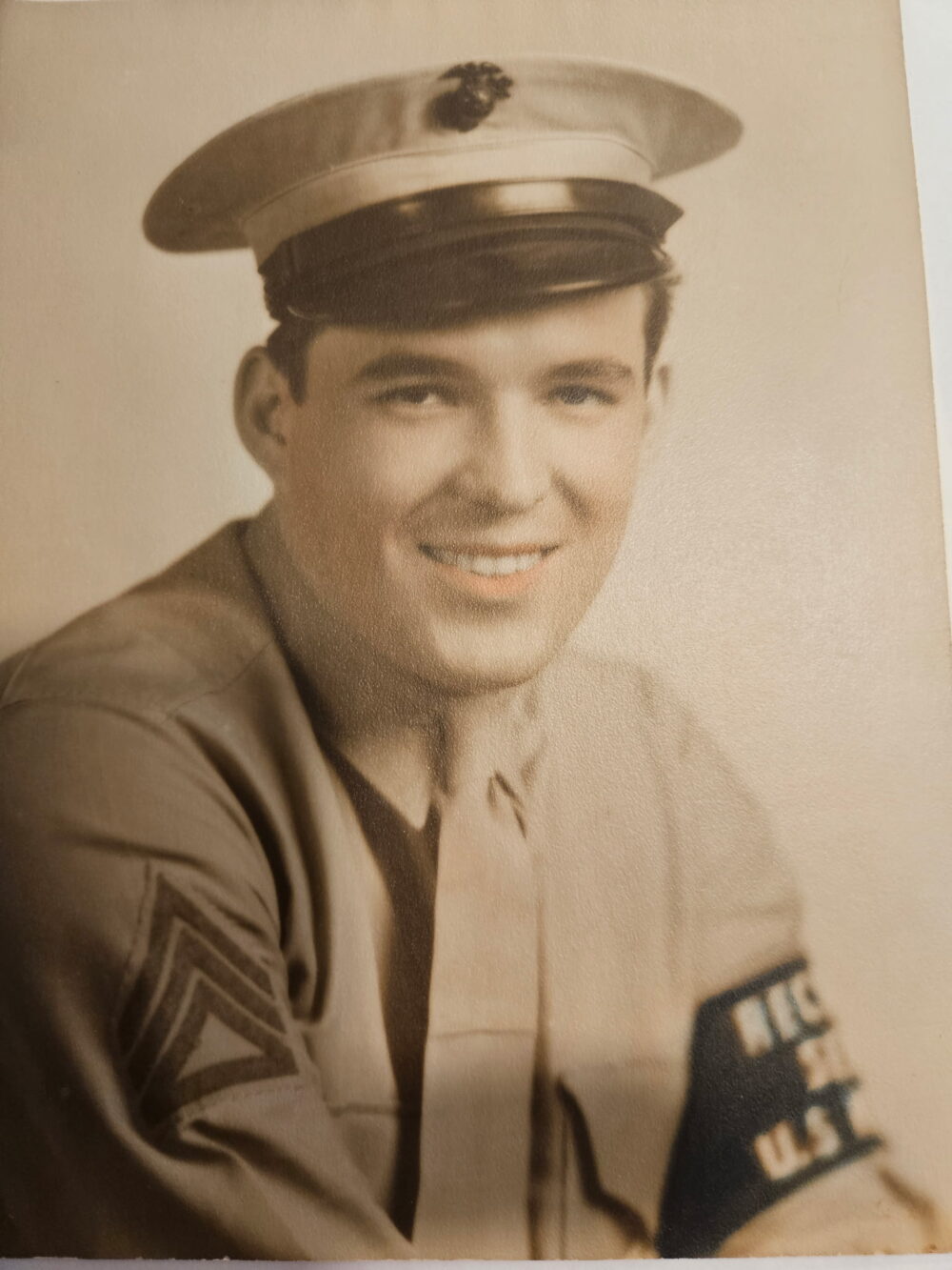 A sepia-toned photograph of a young White man in uniform looking at the camera and smiling. It is taken from the chest up.