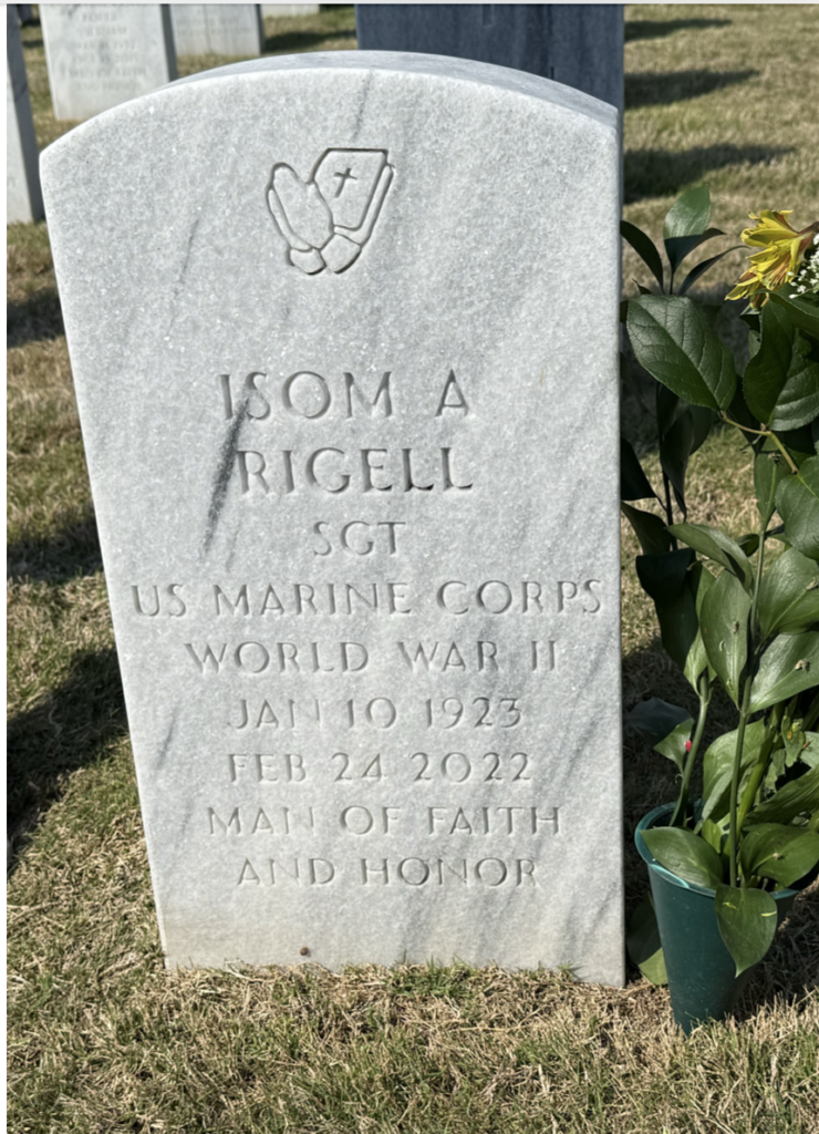 A white marble headstone engraved with "Isom A. Rigell SGT US Marine Corps World War II Jan 10 1923 Feb 24 2022 Man of faith and honor."