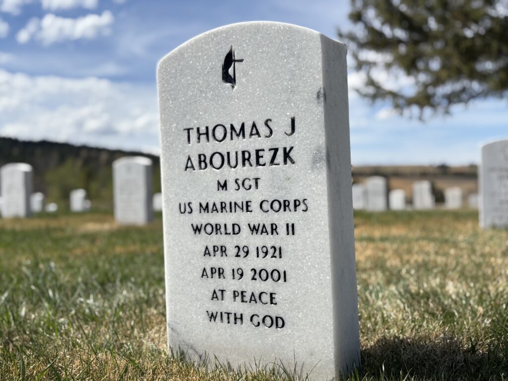 A color photo of an arched white marble headstone engraved with “Thomas J Abourezk M SGT US Marine Corps World War II Apr 29 1921 Apr 19 2001 At peace with God.”