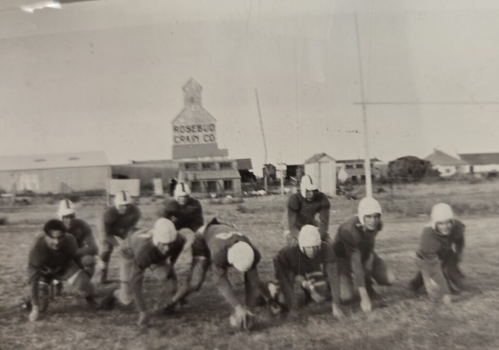 A black and white image of several young men playing football in a field.
