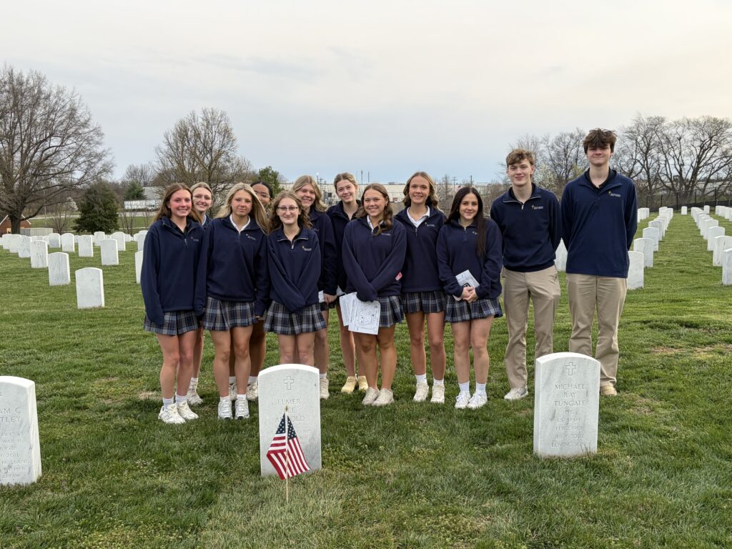 A color photo of several students standing behind a headstone.
