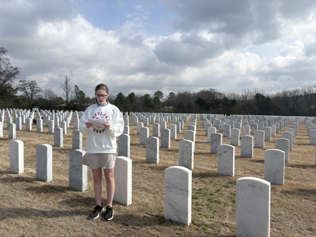 A student stands in a cemetery reading from papers.