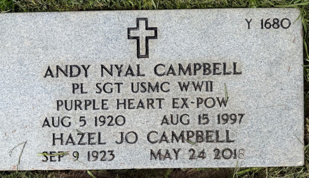 A flat headstone is engraved with a cross and the words, “Andy Nyal Campbell PL SGT USMC WWII Purple Heart EX-POW Aug 5 1920 Aug 15 1997 Hazel Jo Campbell Sep 9 1923 May 24 2018.”