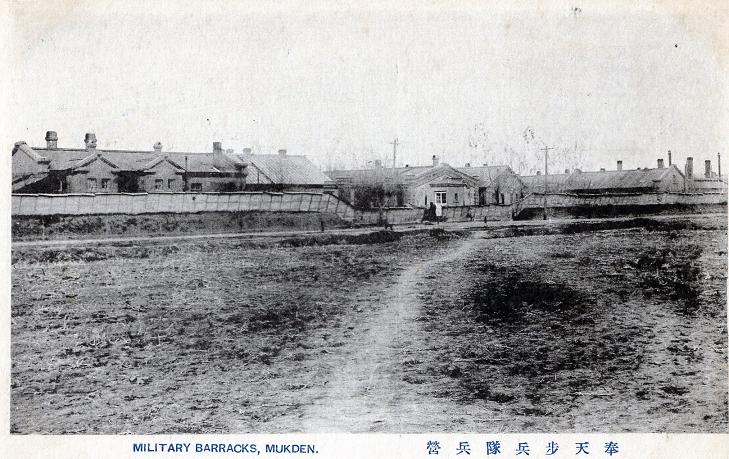 A black and white image of several buildings behind a fence.