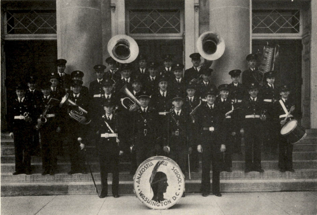 A black and white photo of a large band in uniform standing on the steps outside a building.
