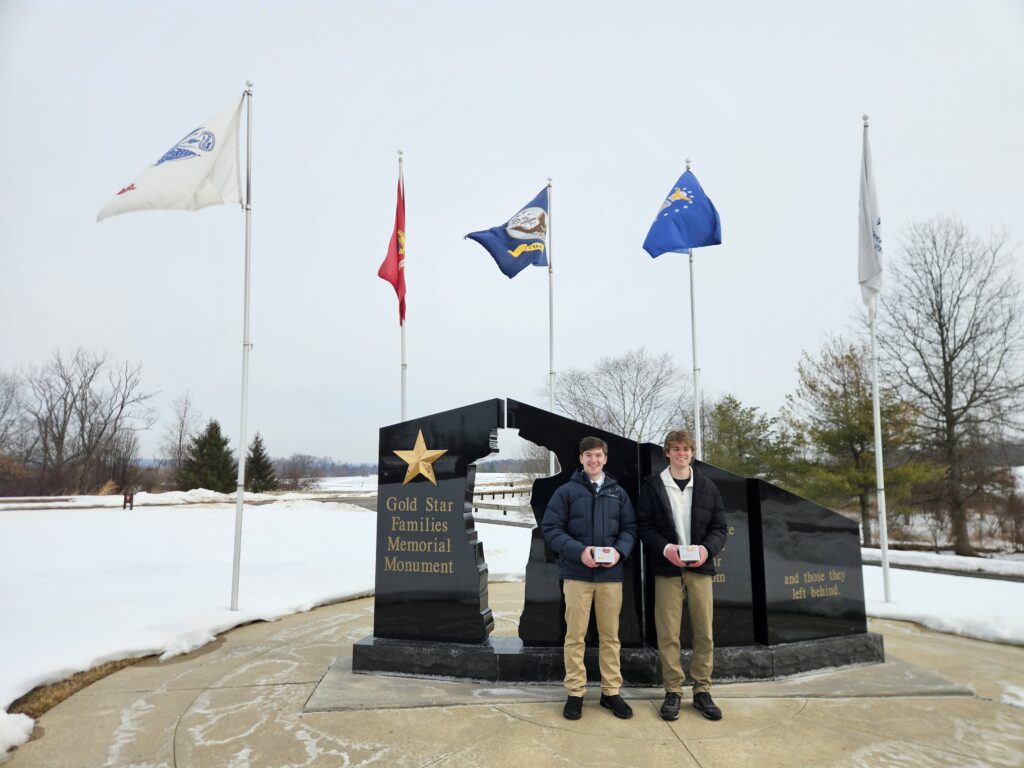 Two young White boys stand in front of a cemetery entrance.