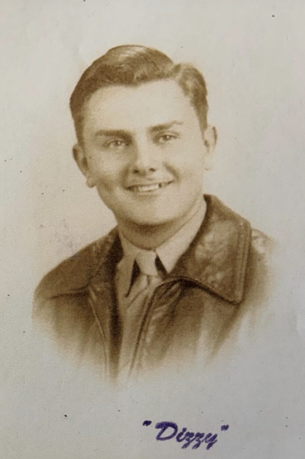 A black and white headshot of a young White man. He is in a button-up uniform shirt and tie with a leather coat on top.