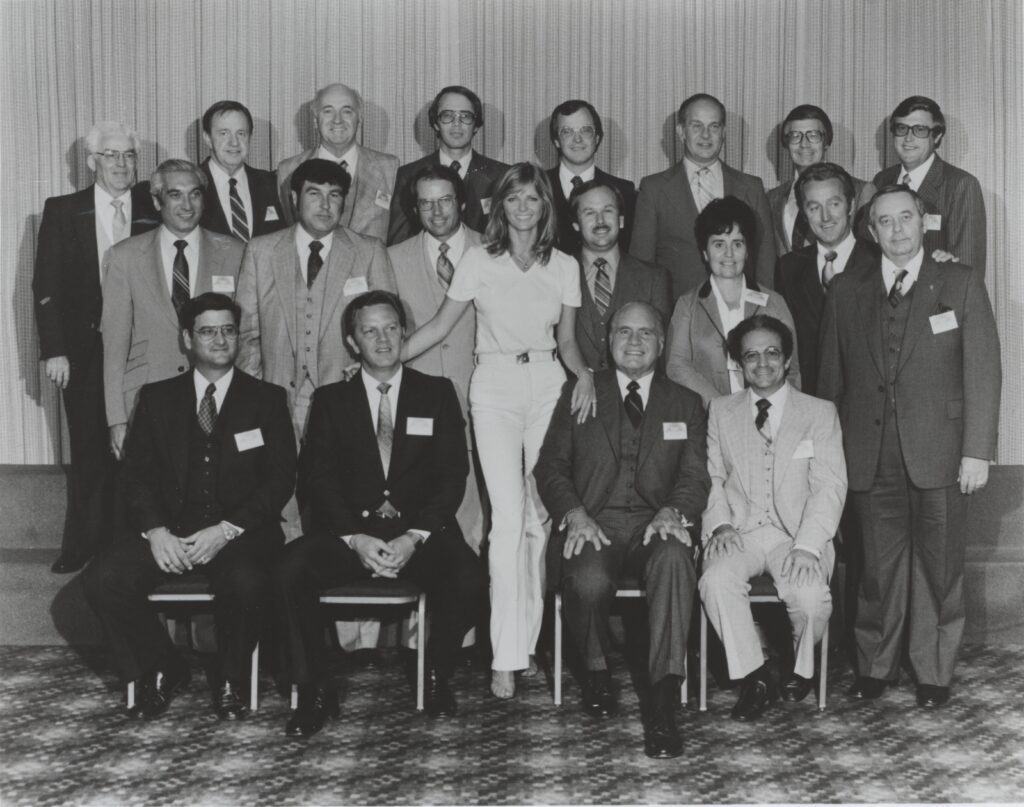 A black and white image of a several people in formal attire posing for a picture.
