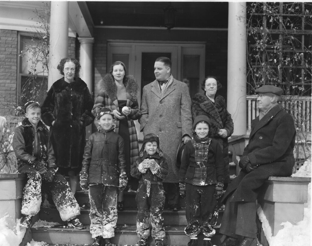 A black and white image of a family with several members of various ages standing outside a home.